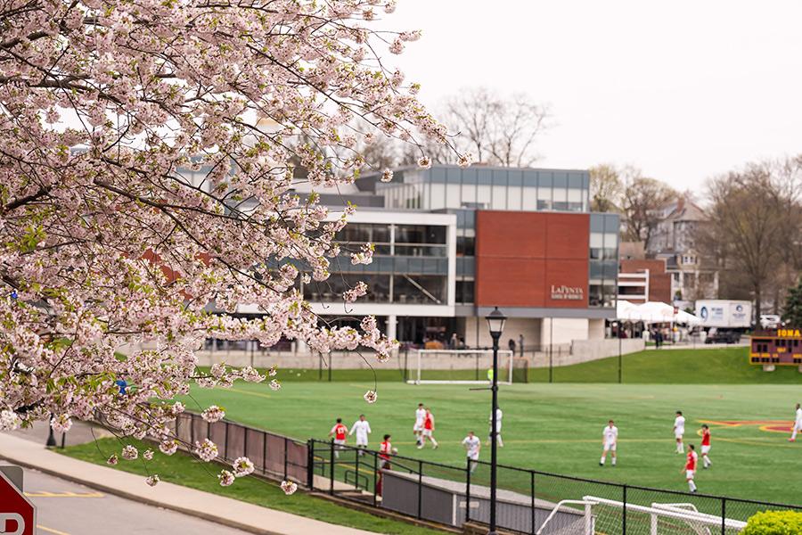 Far side picture of the Iona University's Men Soccer Team game taking place on the Mazzella Field with the LaPenta School of Business behind and in the distance.