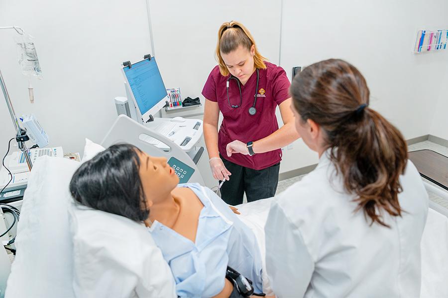Student learning and checking watch, to see mannequin's vitals in a set up hospital room in Iona University.