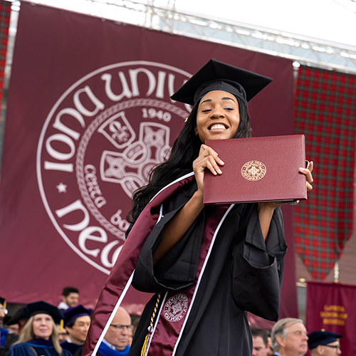 An Iona graduate holds her diploma on stage during Commencement.