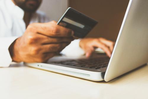 A person holds a credit card in front of a laptop.